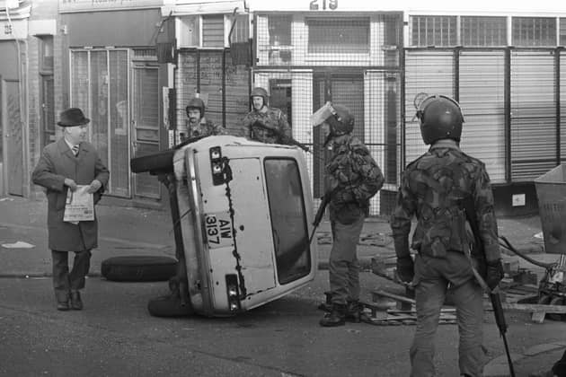 Troops on patrol in the Falls Road area of Belfast encounter a civilian by an overturned car that formed a barricade during rioting in 1981